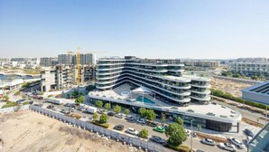 Un immeuble moderne à plusieurs étages, doté d’une façade incurvée, entouré d’un parking et d’un chantier de construction.