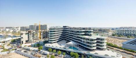 A modern multi-story building with a curved facade, surrounded by a parking lot and a construction site.