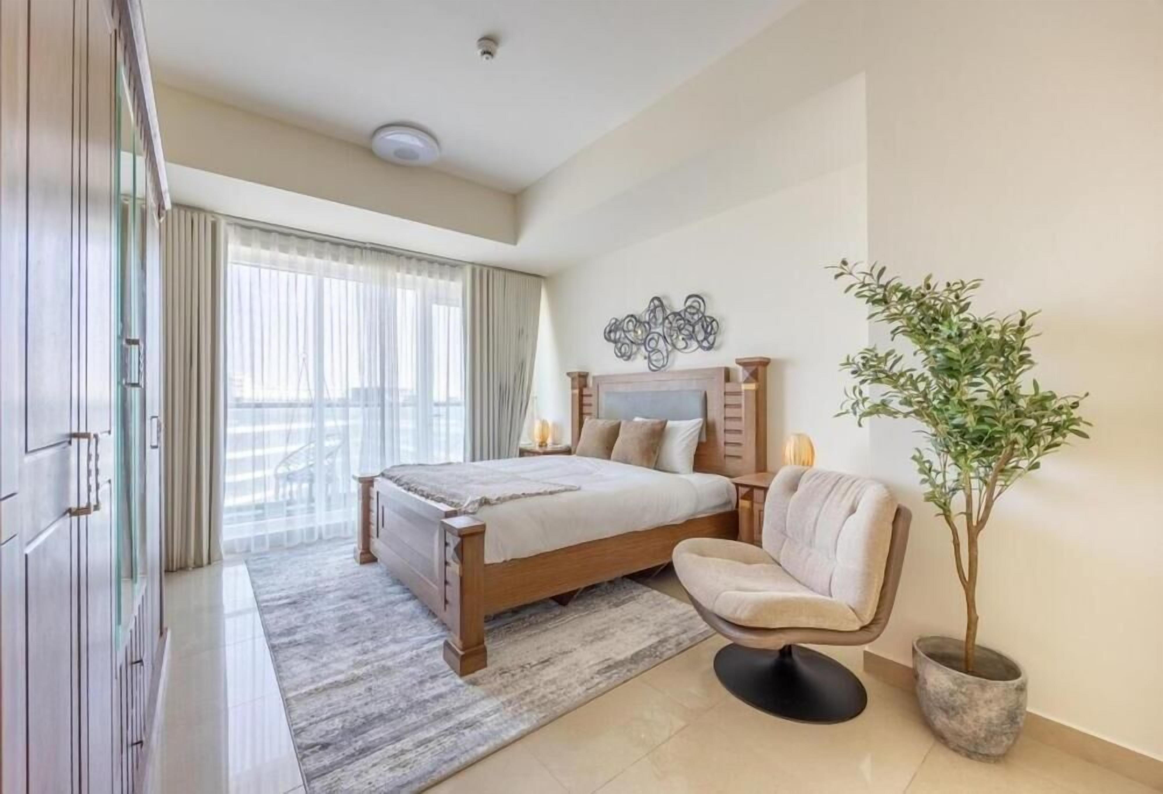 Um quarto com cama, uma cadeira, uma planta em vaso e um objeto decorativo na parede.
