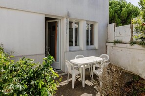Eine kleine Terrasse im Freien mit einem weißen Tisch und Stühlen, einer Betonwand und einer Tür, die zum Innenbereich führt.