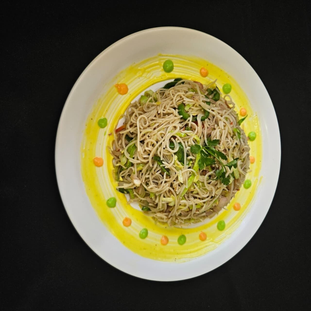 A bowl of noodles with peas and carrots, garnished with herbs, on a white plate with a yellow sauce.