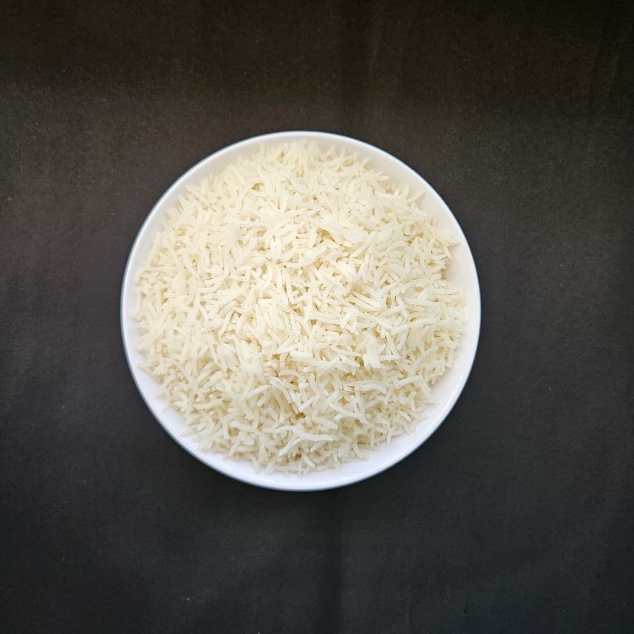 A bowl of white rice on a dark surface.