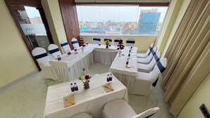 A conference room with a high table and chairs, a view of buildings through the window, and a door with a sign.