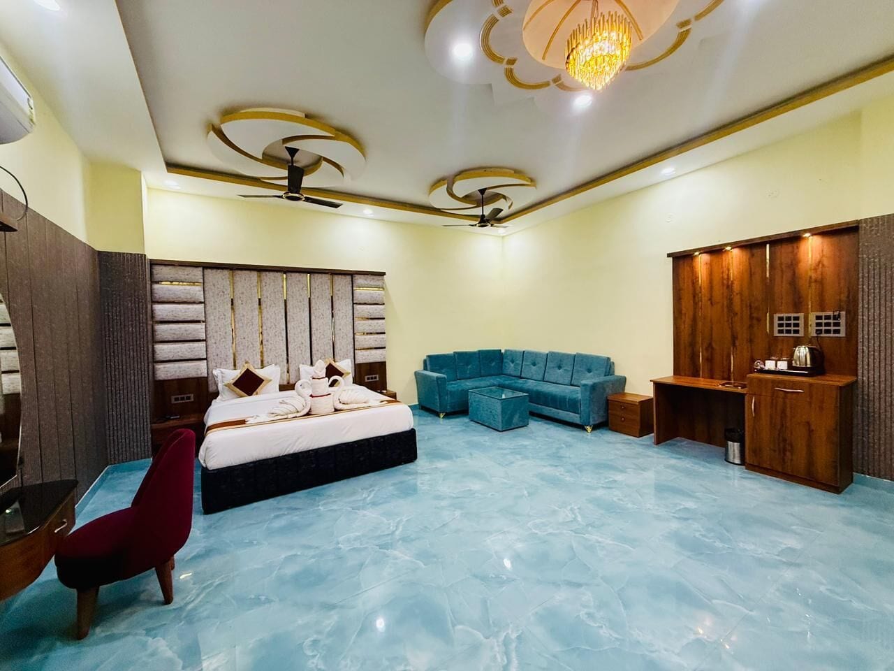 A spacious bedroom with a large bed, a blue sofa, a wooden wardrobe, and a red chair.