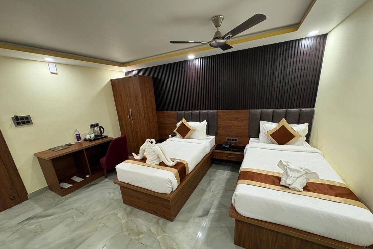 A hotel room with two beds, a desk, a chair, a wardrobe, and a ceiling fan.