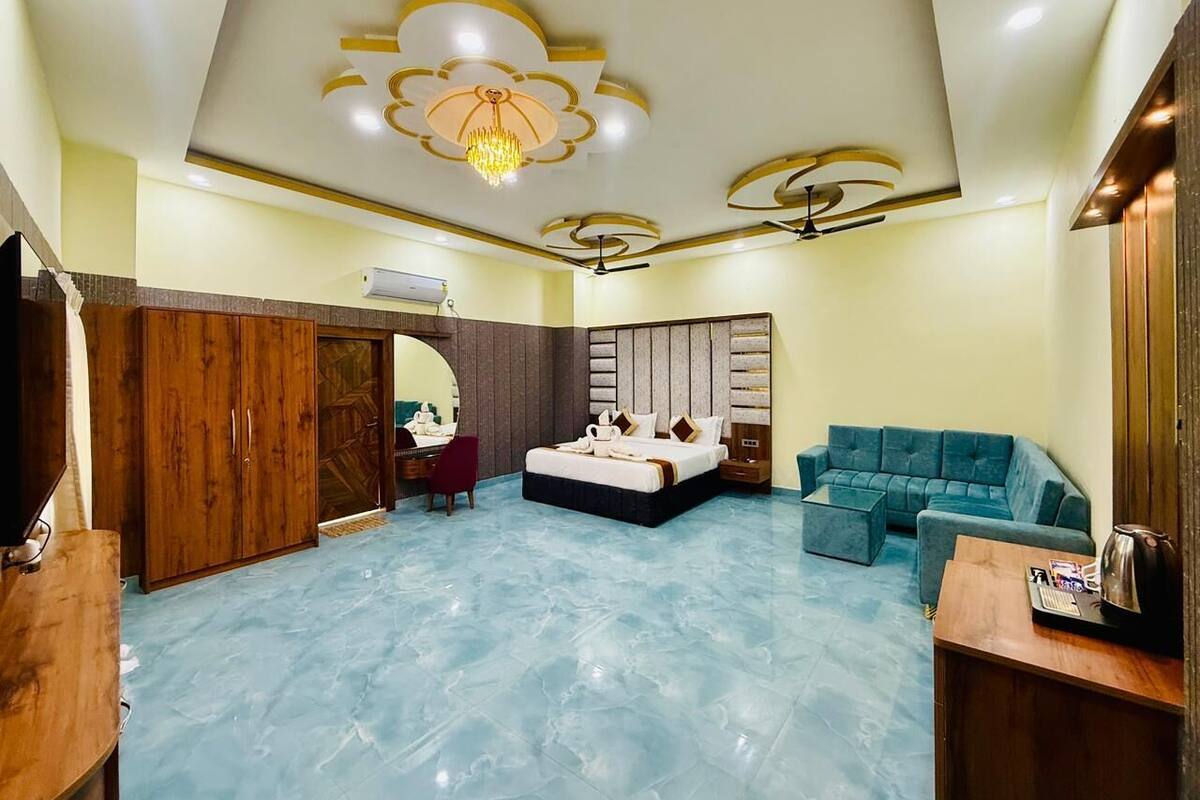 A hotel room with a bed, a blue sofa, a wooden wardrobe, a desk, and a chandelier.