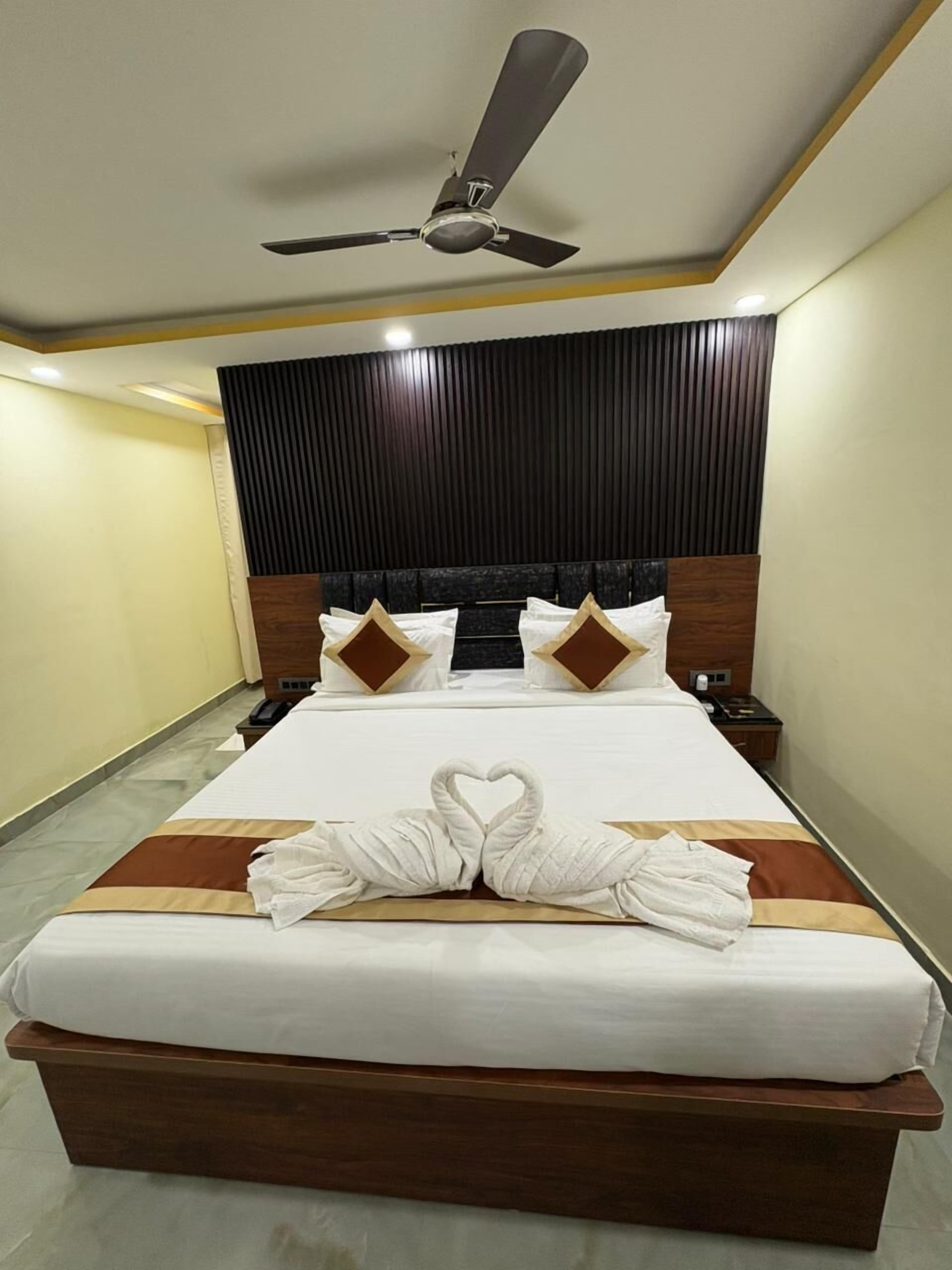 Ein Hotelzimmer mit einem großen Bett, einem Deckenventilator, einem Holzkopfteil und einer herzförmigen Handtuchgestaltung auf dem Bett.