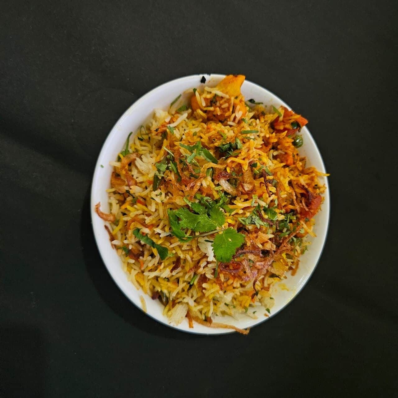 A bowl of biryani with fried onions and cilantro garnish on a dark surface.