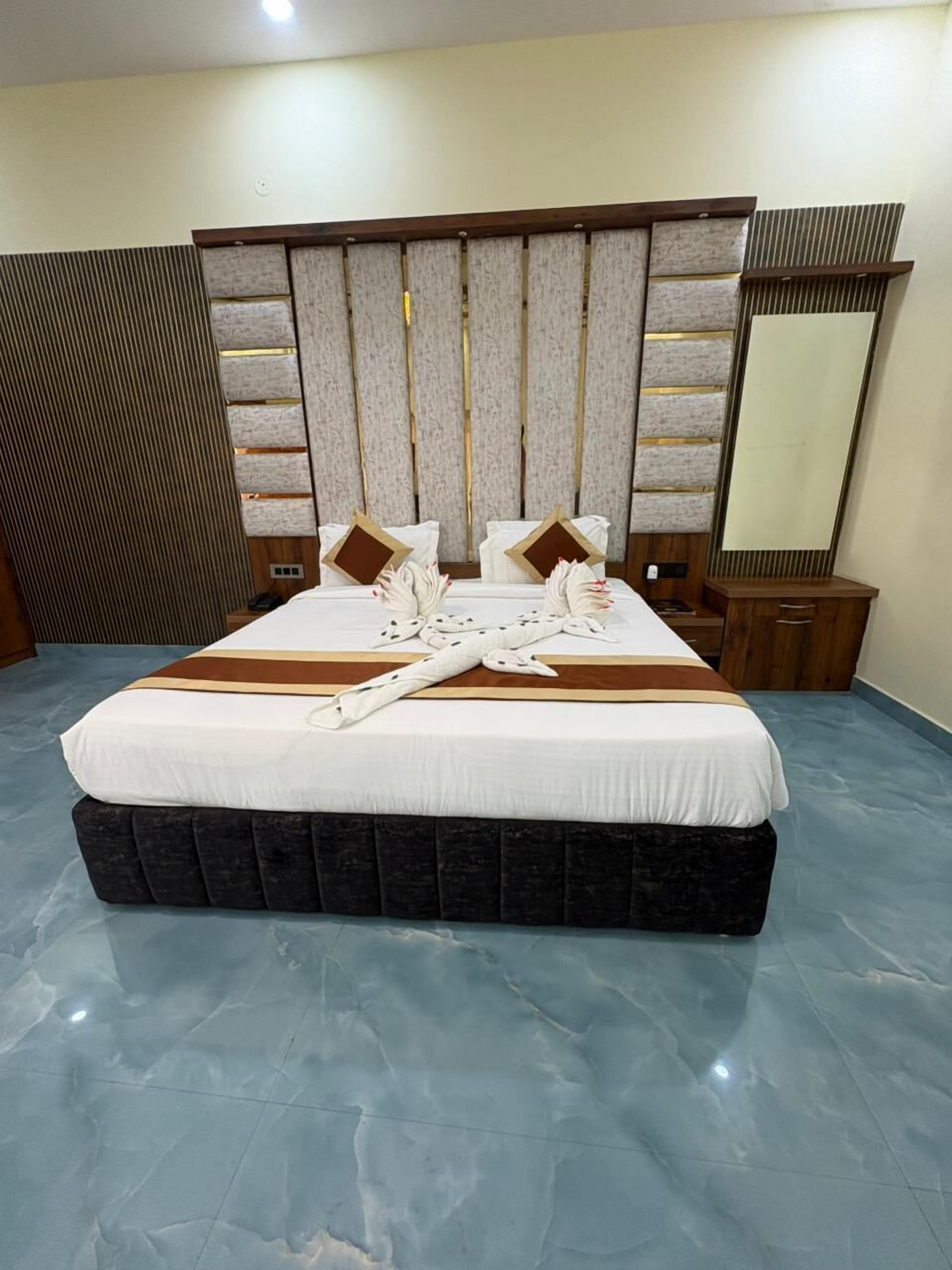 A hotel room with a large bed, a wooden headboard, a mirror, and a bedside table.