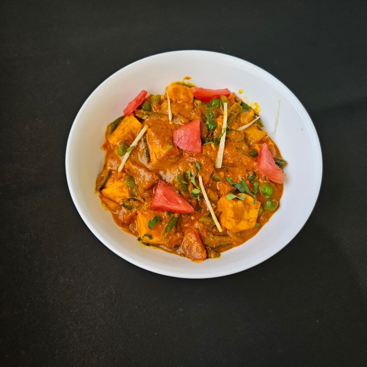Eine Schüssel mit Curry, Paneer und Gemüse.