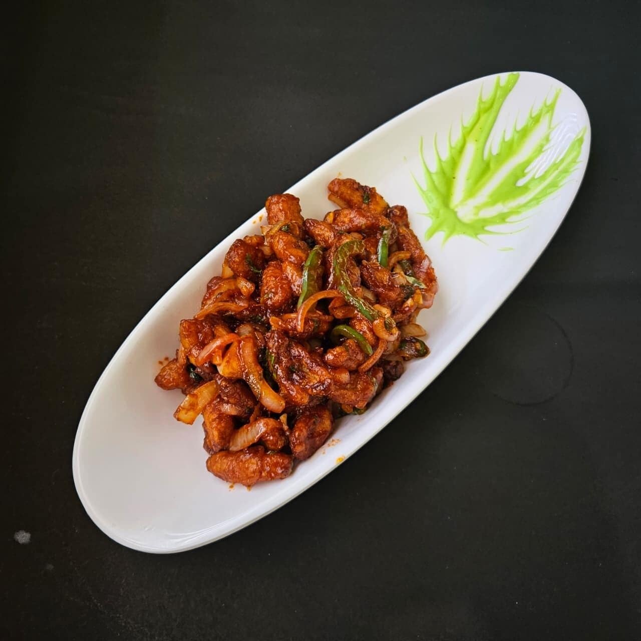 Un plato ovalado blanco con un plato de vegetales salteados, decorado con hojas verdes, sobre una superficie oscura.