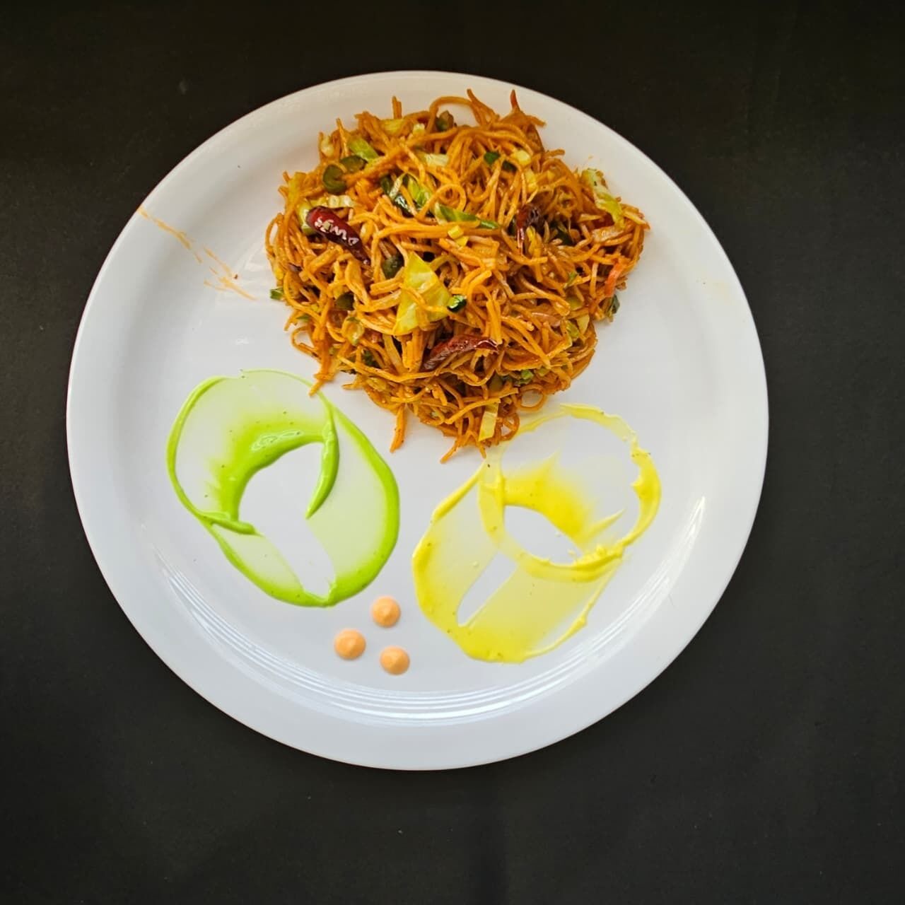 A plate of noodles with green and yellow sauce and peanuts on a white plate.