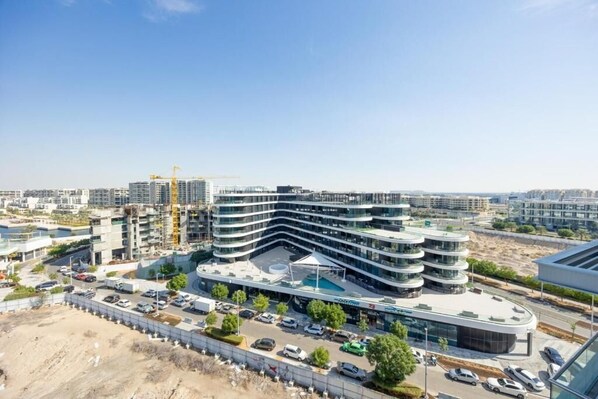 A modern multi-story building with a curved facade, surrounded by a parking lot and a construction site. - Unit 805 Jamam Residence (Abu Dhabi)