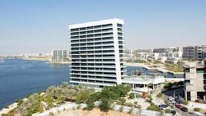 A modern high-rise hotel with multiple balconies, situated near a waterfront with palm trees and a sandy beach. - Unit 805 Jamam Residence (Abu Dhabi)