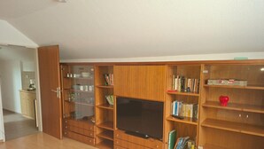 Tilava olohuone, jossa on suuri puinen mediakeskus, litteänäyttöinen televisio ja avoimen oven kautta näkyvä keittiöalue.