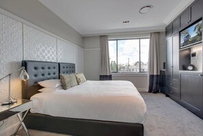 A hotel room with a large bed, a TV, a desk with a lamp, and a view of the city through the window. - Perfect Located 2-Bed Blue Mountains Getaway (Katoomba)