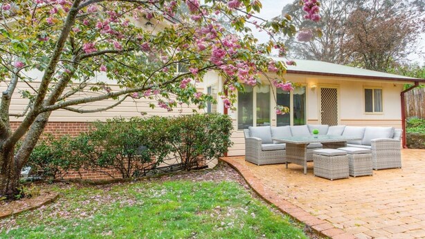 A house with a patio area featuring outdoor furniture and a tree with pink blossoms. - Stunning Katoomba Home with Lush Garden&Playground (Katoomba)