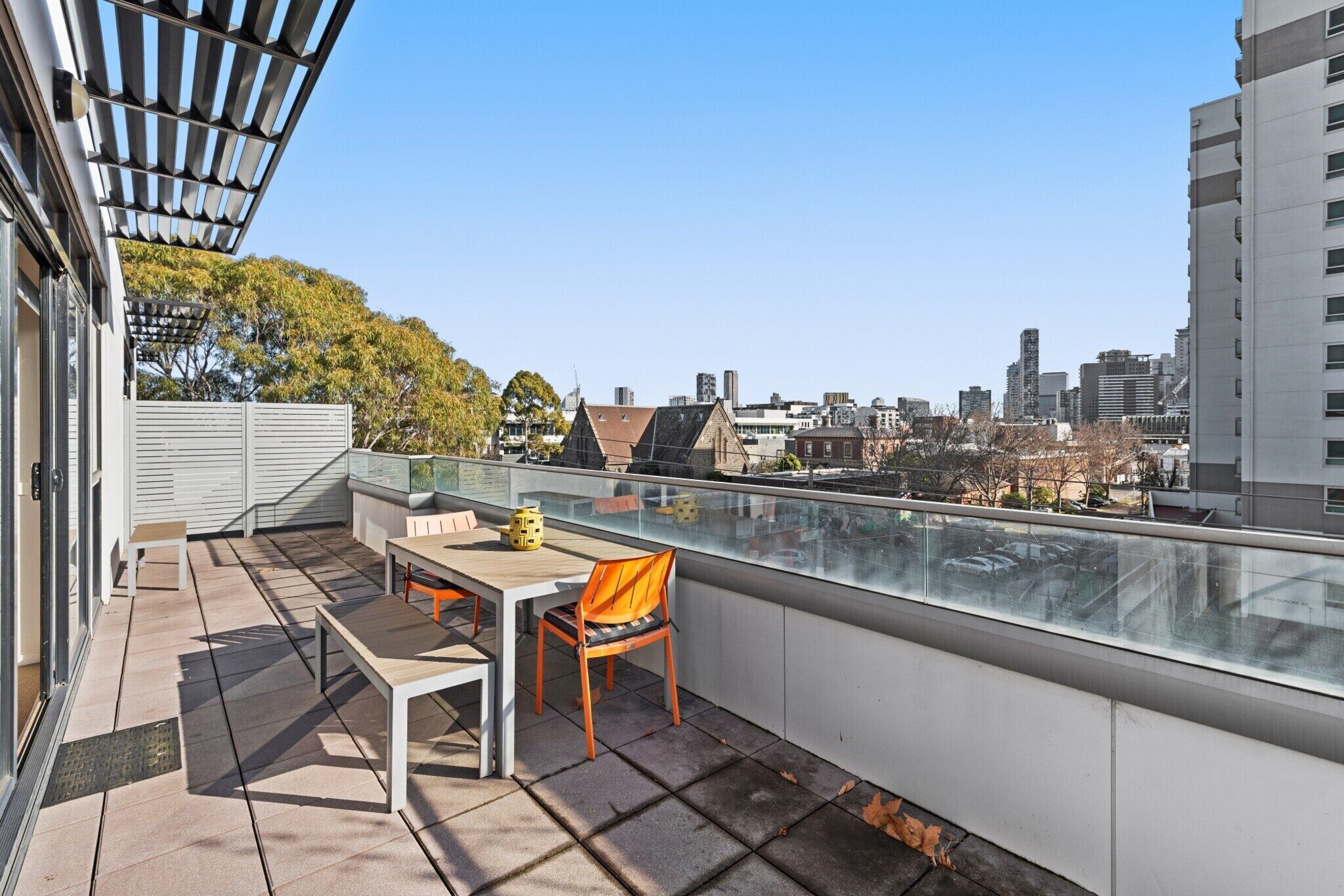 A rooftop terrace with a table and chairs, a pergola, and a city view.