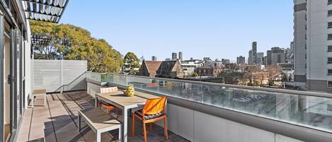A rooftop terrace with a table and chairs, a pergola, and a city view.