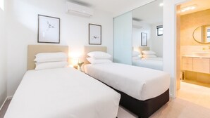 Une chambre d ’hôtel avec deux lits, un grand miroir, une salle de bain avec un lavabo et un miroir, et des œuvres d’art encadrées accrochées aux murs.
