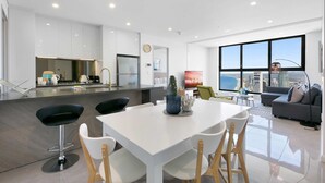 Una sala de estar moderna con una mesa de comedor blanca, taburetes negros y un sofá gris.