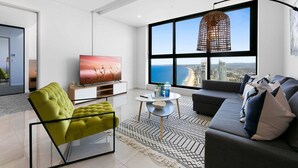 Una sala moderna con un ventanal grande, un sofá, un sillón verde, un televisor y una lámpara colgante decorativa.