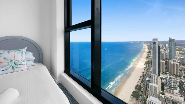 Un dormitorio con un ventanal grande que da a la playa y al paisaje urbano.