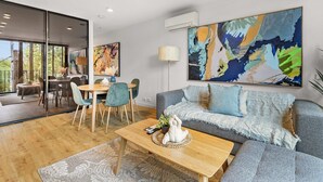 Een moderne woonkamer met een grijze bank, een houten salontafel en een eethoek met een tafel en stoelen.