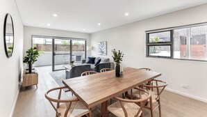 Un comedor moderno con una mesa y sillas de madera, un ventanal con vistas al exterior y una puerta corrediza de vidrio que da a un balcón.