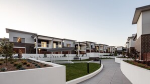 Un moderno complejo residencial con varias casas de dos pisos, un sendero central y jardines ajardinados.