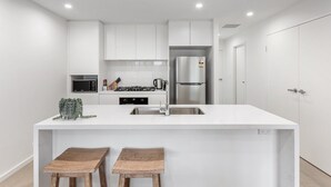 Una cocina moderna con armarios blancos, un refrigerador de acero inoxidable y una isla central con taburetes.
