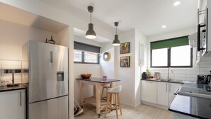 Une cuisine moderne avec un réfrigérateur en acier inoxydable, des tabourets de bar en bois, une petite table à manger et des luminaires suspendus.
