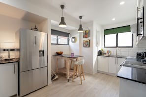 Een moderne keuken met een roestvrijstalen koelkast, houten barkrukken, een eettafeltje en hanglampen.
