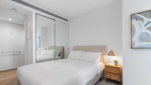Ein modernes Schlafzimmer mit einem großen Bett, einem Nachttisch mit Lampe und einer Schiebetür zum Kleiderschrank.