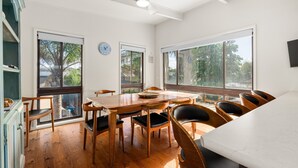 A dining area with a wooden table and chairs, large windows, and a ceiling fan. - Spacious 4-Bed Home 5-min from the Beach (Capel Sound)