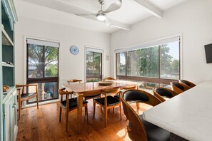 A dining area with a wooden table and chairs, large windows, and a ceiling fan. - Spacious 4-Bed Home 5-min from the Beach (Capel Sound)