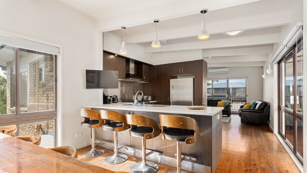 A modern kitchen with a central island, bar stools, and a dining table. - Spacious 4-Bed Home 5-min from the Beach (Capel Sound)
