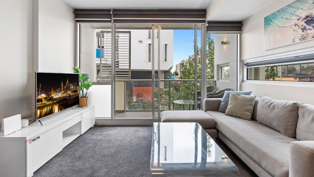 A modern living room with a large TV, a sofa, a coffee table, and a balcony with a view of the city. - Fitzroy North 1-Bed with Balcony by Edinburgh Park (Fitzroy North)