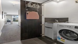 A compact laundry room with a Bosch washing machine, a dark wooden door, and a towel rack with a patterned towel. - Fitzroy North 1-Bed with Balcony by Edinburgh Park (Fitzroy North)