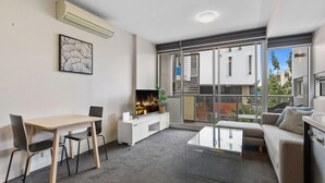 A modern living room with a dining area, a sofa, a coffee table, and a TV. - Fitzroy North 1-Bed with Balcony by Edinburgh Park (Fitzroy North)