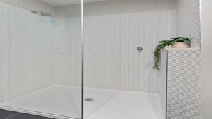A modern shower enclosure with a glass door, a white tiled wall, and a small potted plant on a shelf. - Fitzroy North 1-Bed with Balcony by Edinburgh Park (Fitzroy North)