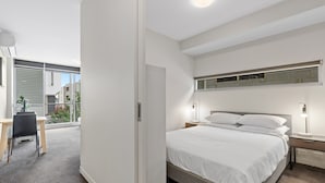 A modern bedroom with a large bed, bedside tables, a desk, and a view of the outside. - Fitzroy North 1-Bed with Balcony by Edinburgh Park (Fitzroy North)