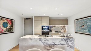 A modern kitchen with a marble island, built-in appliances, and artwork on the walls. - Jewel Luxury Beachside 2-Bed with Water View (Surfers Paradise)