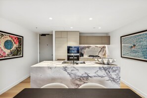 A modern kitchen with a marble island, built-in appliances, and artwork on the walls. - Jewel Luxury Beachside 2-Bed with Water View (Surfers Paradise)