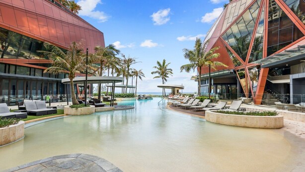 A modern hotel with a pool area, palm trees, and a clear sky. - Jewel Luxury Beachside 2-Bed with Water View (Surfers Paradise)