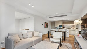 A modern living room with a grey sofa, a white armchair, a marble coffee table, and a kitchen area in the background. - Jewel Luxury Beachside 2-Bed with Water View (Surfers Paradise)