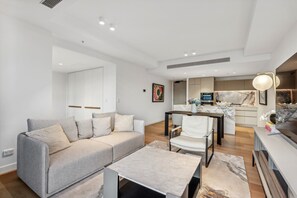 A modern living room with a grey sofa, a white armchair, a marble coffee table, and a kitchen area in the background. - Jewel Luxury Beachside 2-Bed with Water View (Surfers Paradise)