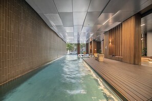 Ein moderner, überdachter Schwimmbereich mit Holzterrasse und gefliesten Wänden.