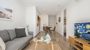 A modern living room with a grey sofa, a glass coffee table, and a painting of Van Gogh's 'Starry Night' on the wall. - 1BR Apartment Near CBD with Pool (Docklands)