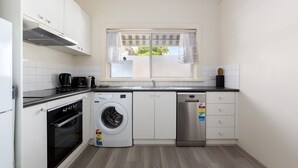 Een kleine keuken met witte kastjes, een inbouwoven, een wasmachine en een vaatwasser.